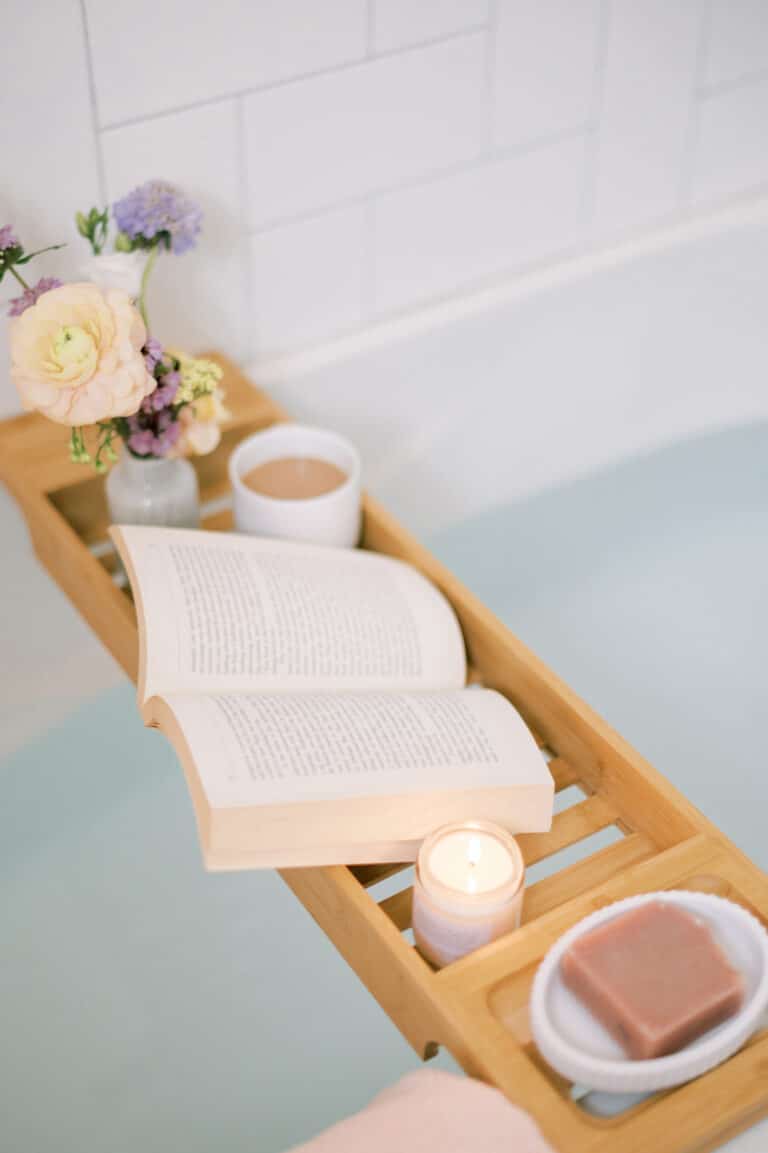 Simple indulgences that help you live a luxury lifestyle on a budget—a warm bath, tea, book, candle, and fresh flowers in a cozy setting.