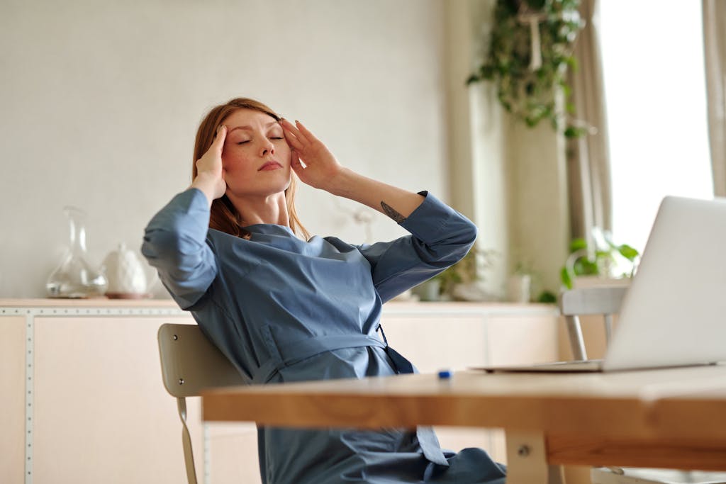 Woman experiencing headache at work, sitting at desk with a laptop, indoors.