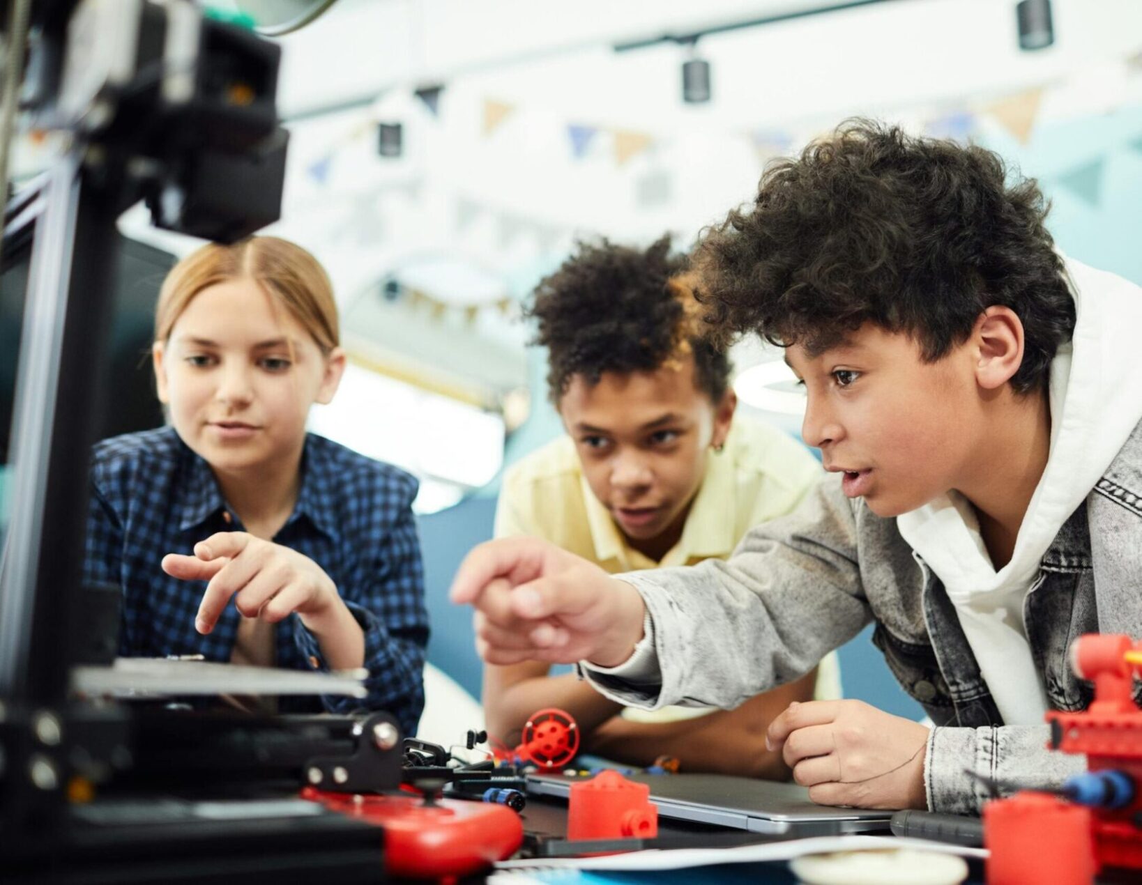 Three teenagers focused on a STEM project using a 3D printer in a collaborative indoor setting.