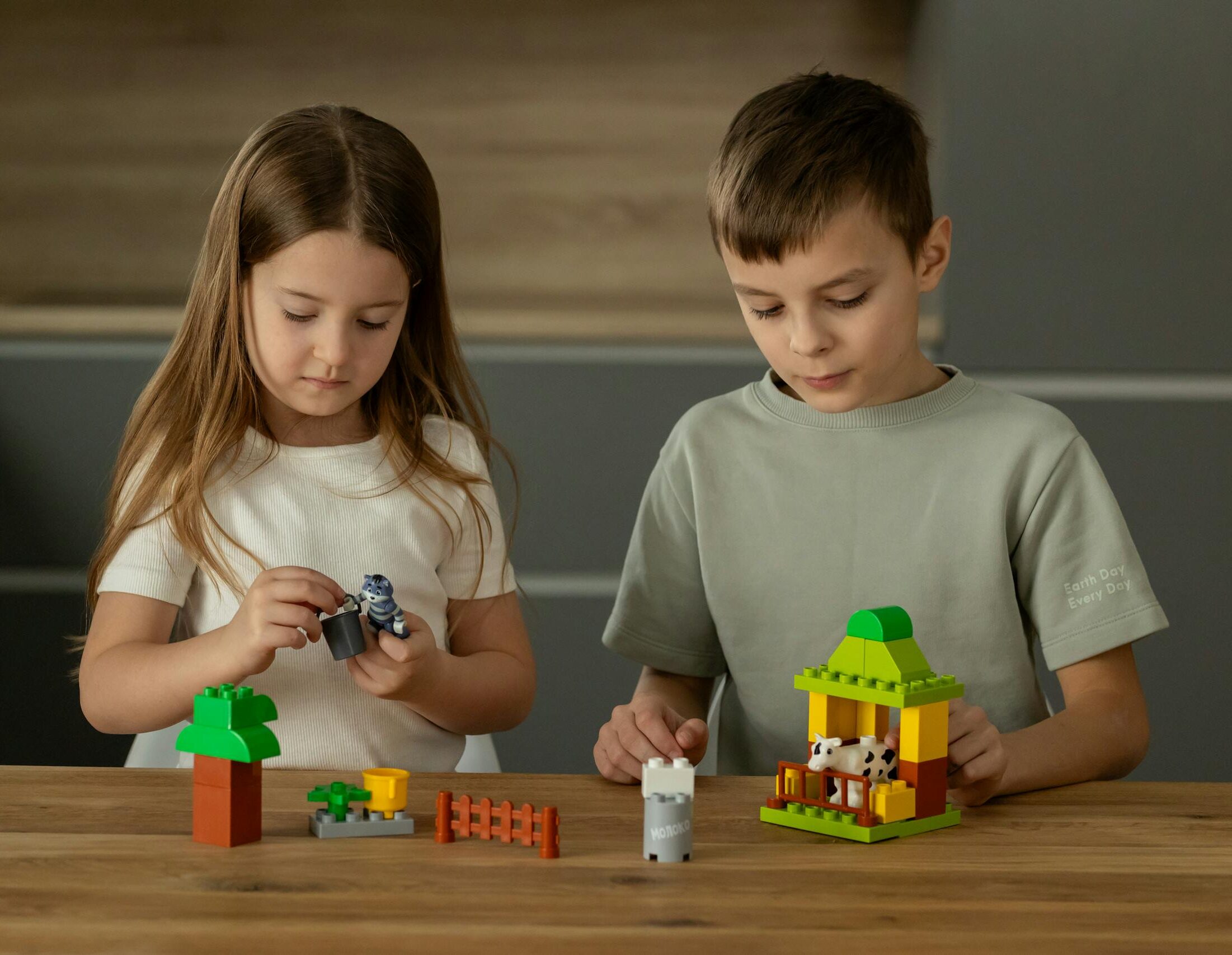 Two young children playing Legos and assembling toys on a wooden table, fostering creativity.